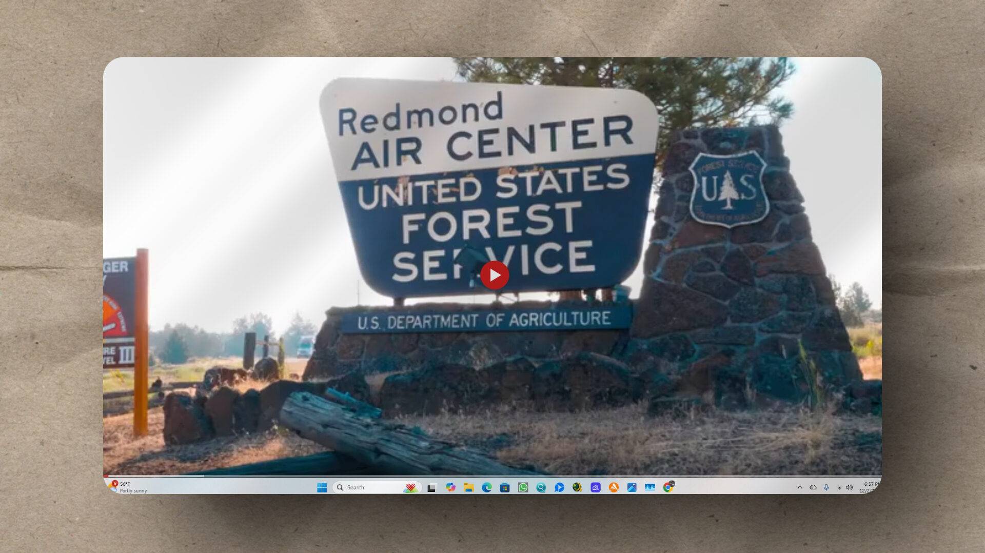 A sign reading "Redmond Air Center, United States Forest Service, U.S. Department of Agriculture" stands next to a stone pillar with a Forest Service shield, set in a rural outdoor area.