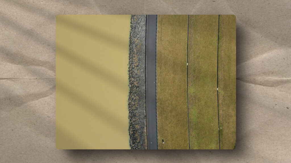 Aerial view of a dam illustrating a structural boundary. A rocky breakwater and road act as an interface between fluid water and terraced land.