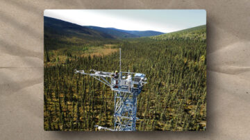 A tall metal tower stands above a dense forest of evergreen trees, with mountains in the distance. The tower supports scientific equipment and two people working, surrounded by a vast, green landscape under a clear sky.