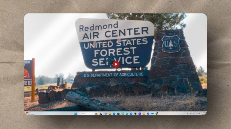 A sign reading "Redmond Air Center, United States Forest Service, U.S. Department of Agriculture" stands next to a stone pillar with a Forest Service shield, set in a rural outdoor area.